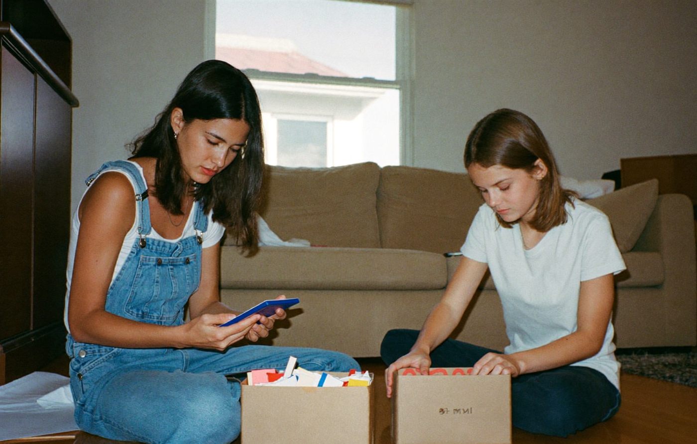A mother and her teenage daughter packing belongings into boxes